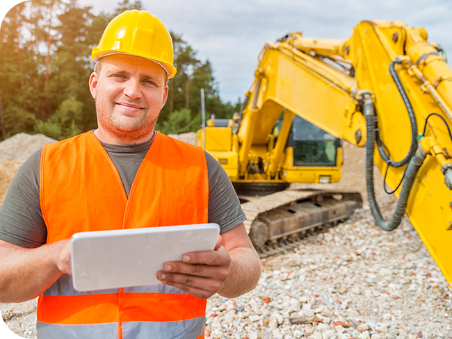Construction worker standing on a worksite, checking business credit line requirements on a tablet.